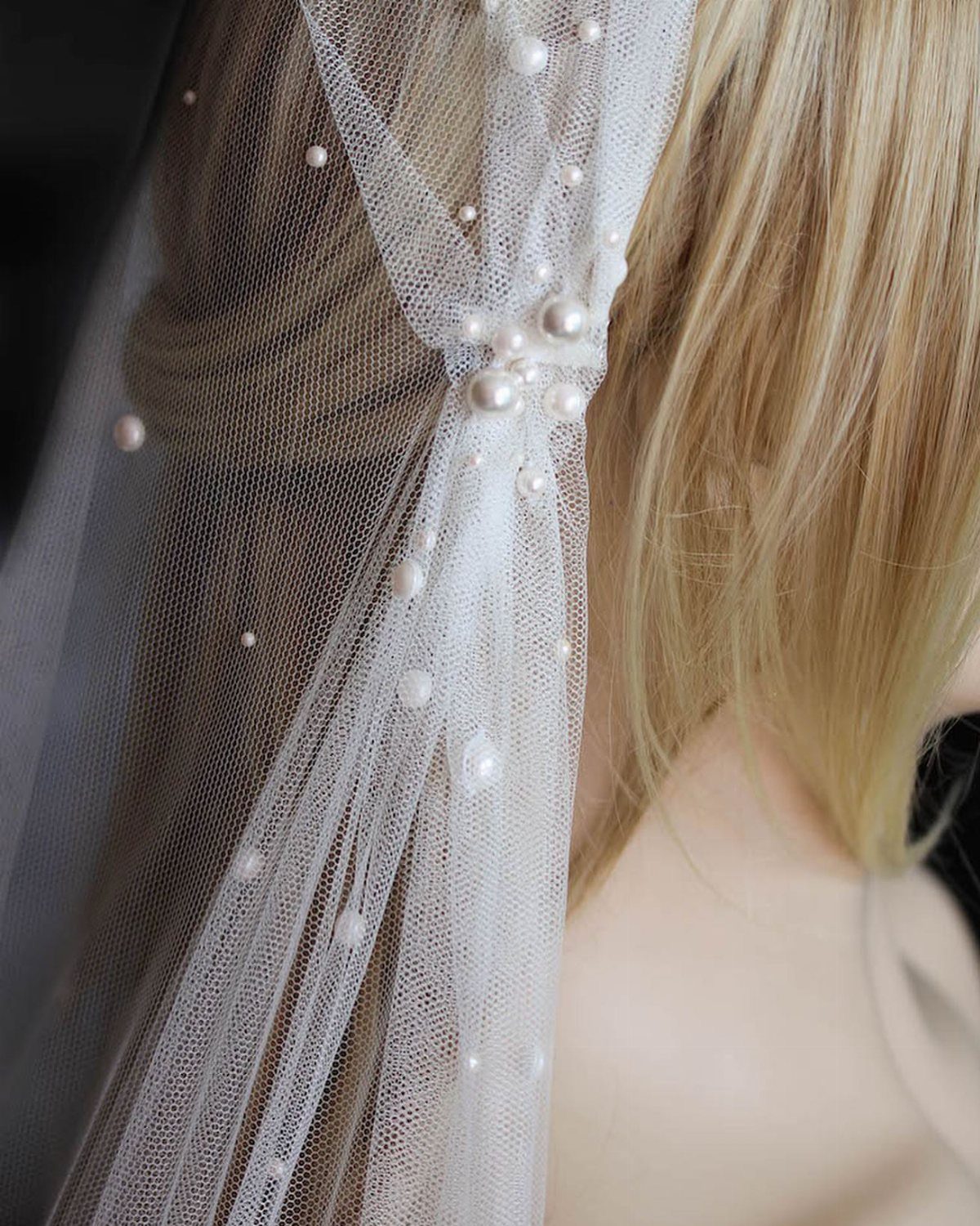 White tulle wedding veil decorated with small pearls draped over blonde hair.