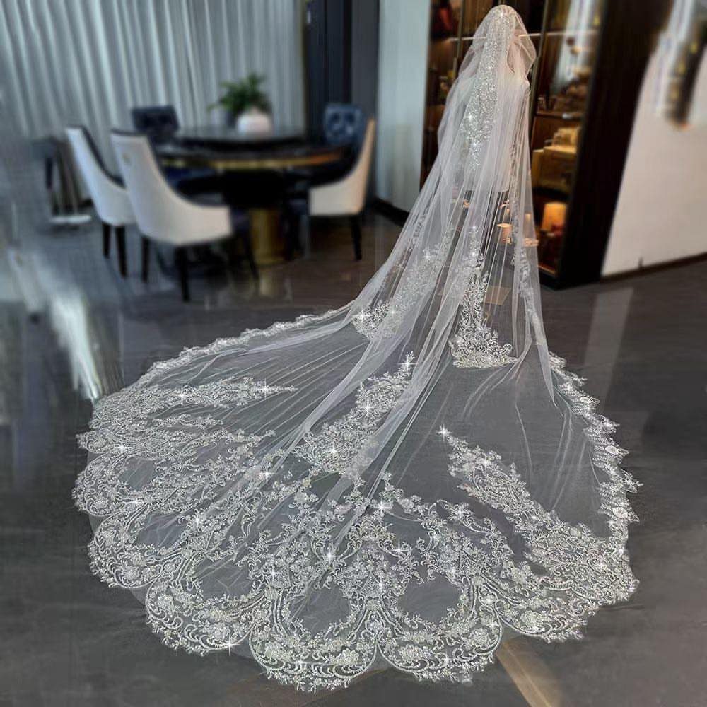 A long, ornate lace cathedral wedding veil spread out on a dark reflective floor.