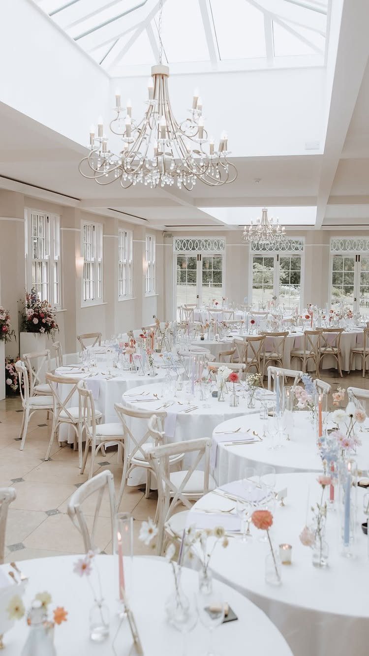Round wedding tables with white linens and floral centerpieces in a bright ballroom.