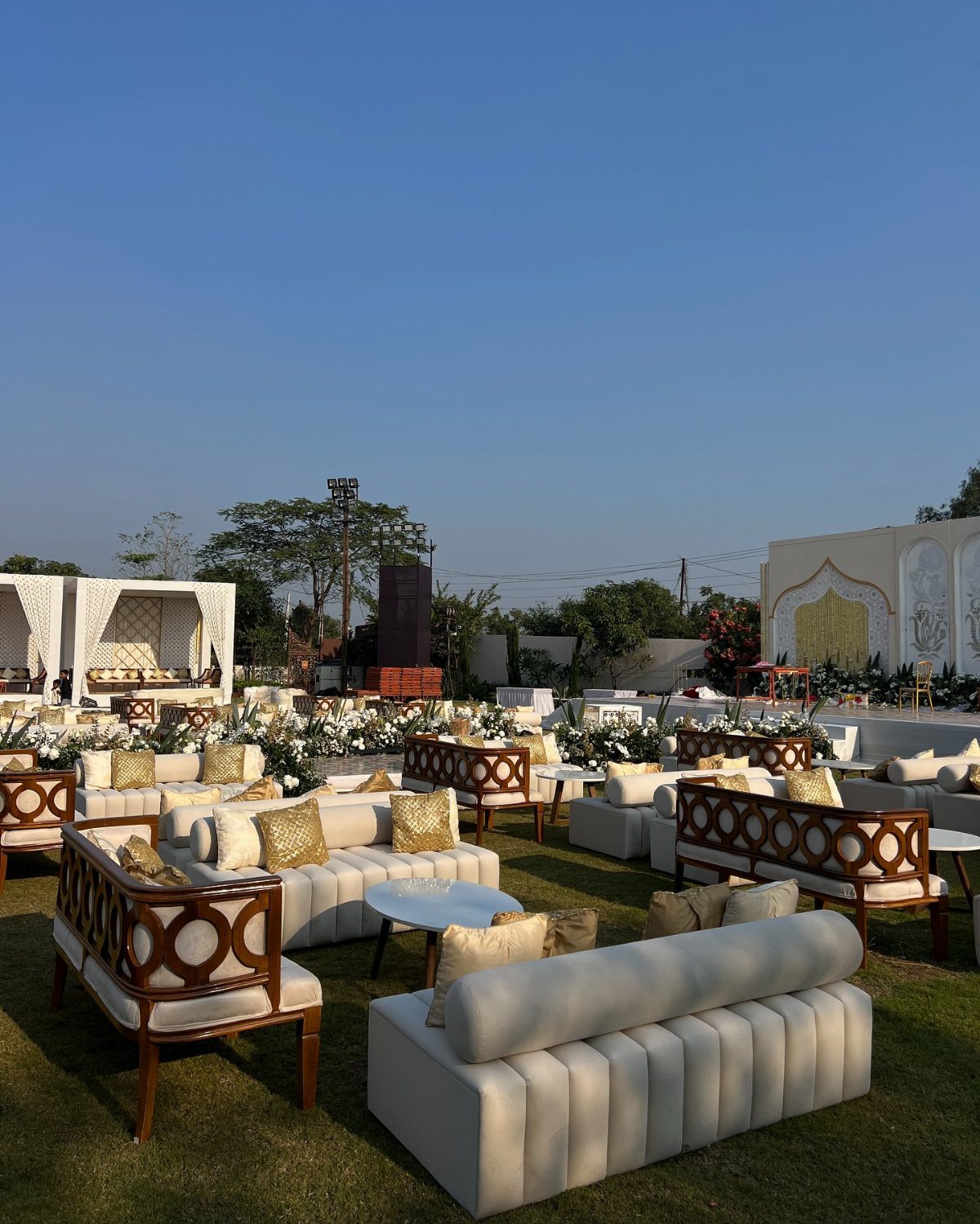 White lounge sofas and wooden armchairs arranged around small tables on a green lawn.