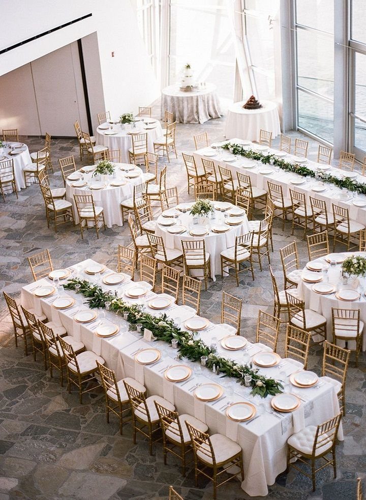 Wedding reception hall featuring a mix of long rectangular and round tables with white linens and greenery.
