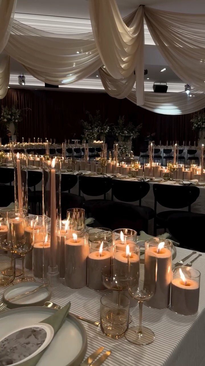 Numerous lit pillar candles in glass holders arranged on a long wedding reception table.