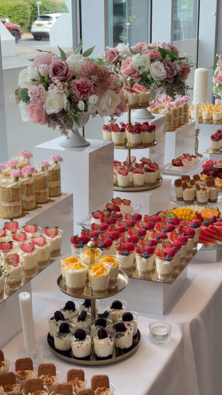 Various small dessert parfaits and treats arranged on a white tiered wedding dessert table.