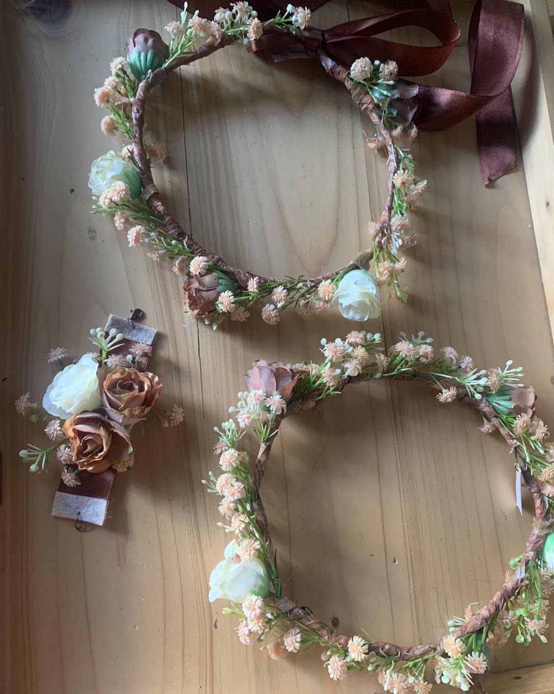 Two floral crowns and a small hair accessory resting on a wooden surface.