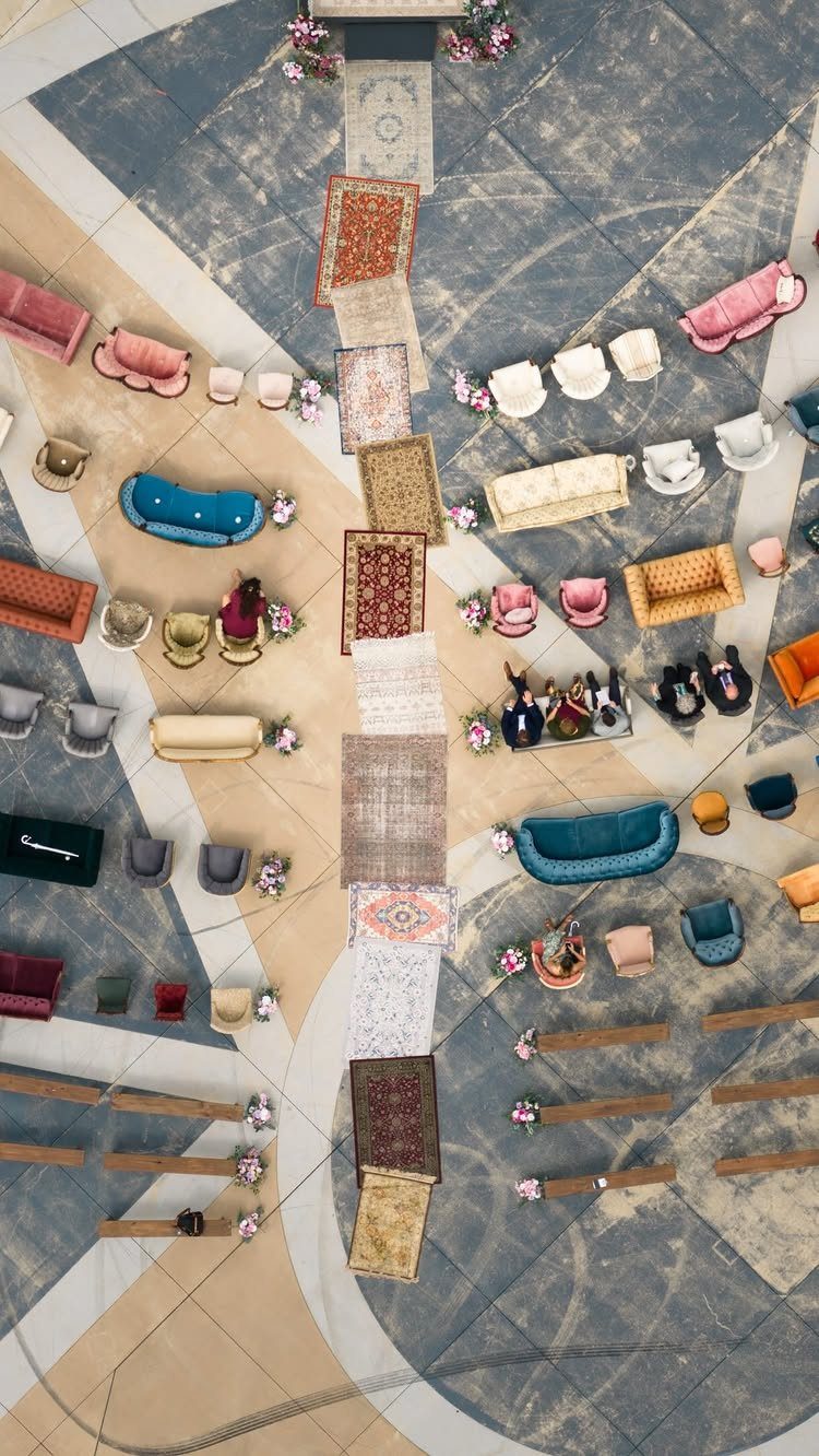 Mismatched vintage sofas and rugs arranged in a geometric pattern on a tiled courtyard floor.