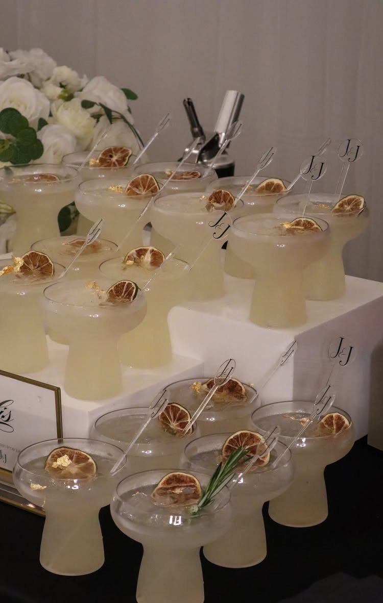 Pale yellow cocktails garnished with dried citrus slices arranged on white tiered stands.