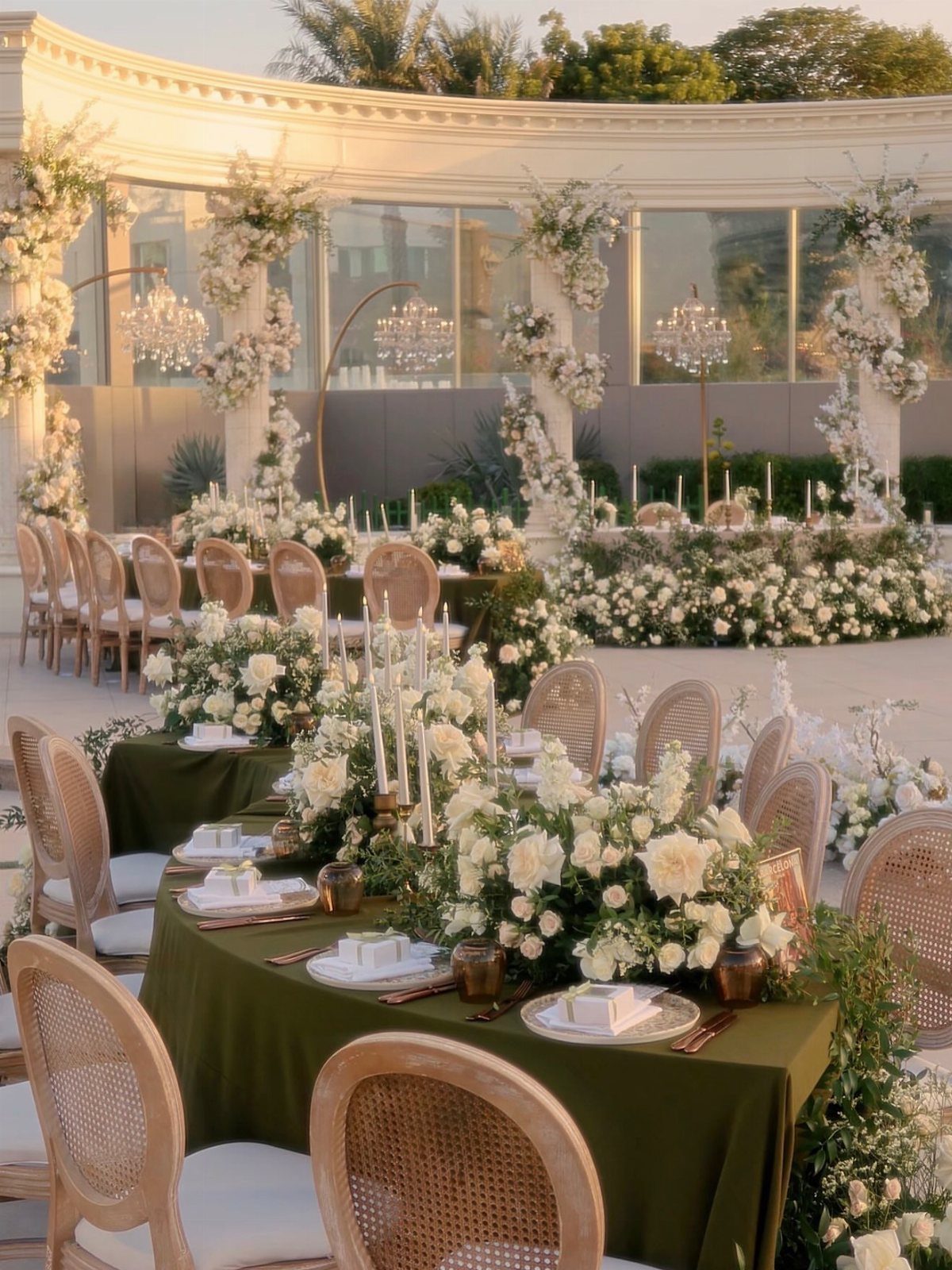 Elegant outdoor wedding tablescapes featuring green linens, white flowers, and tall taper candles.