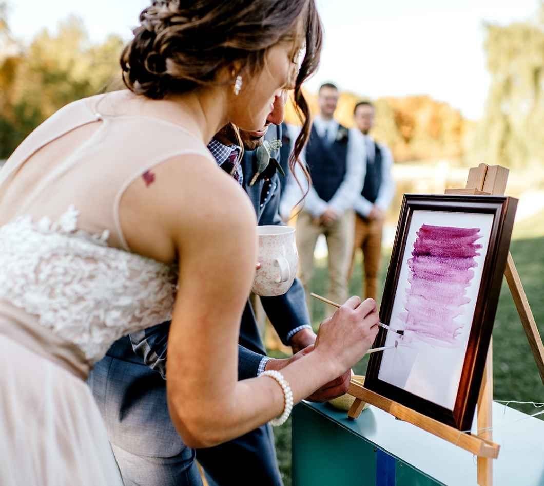 A bride and groom painting colorful strokes on a canvas set upon a wooden easel.