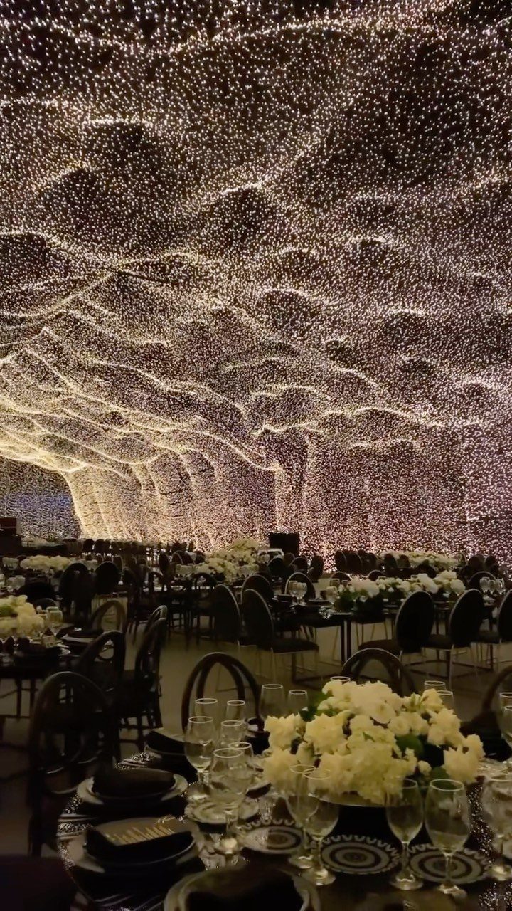 Thousands of tiny warm white fairy lights forming a wavy canopy over a banquet hall.