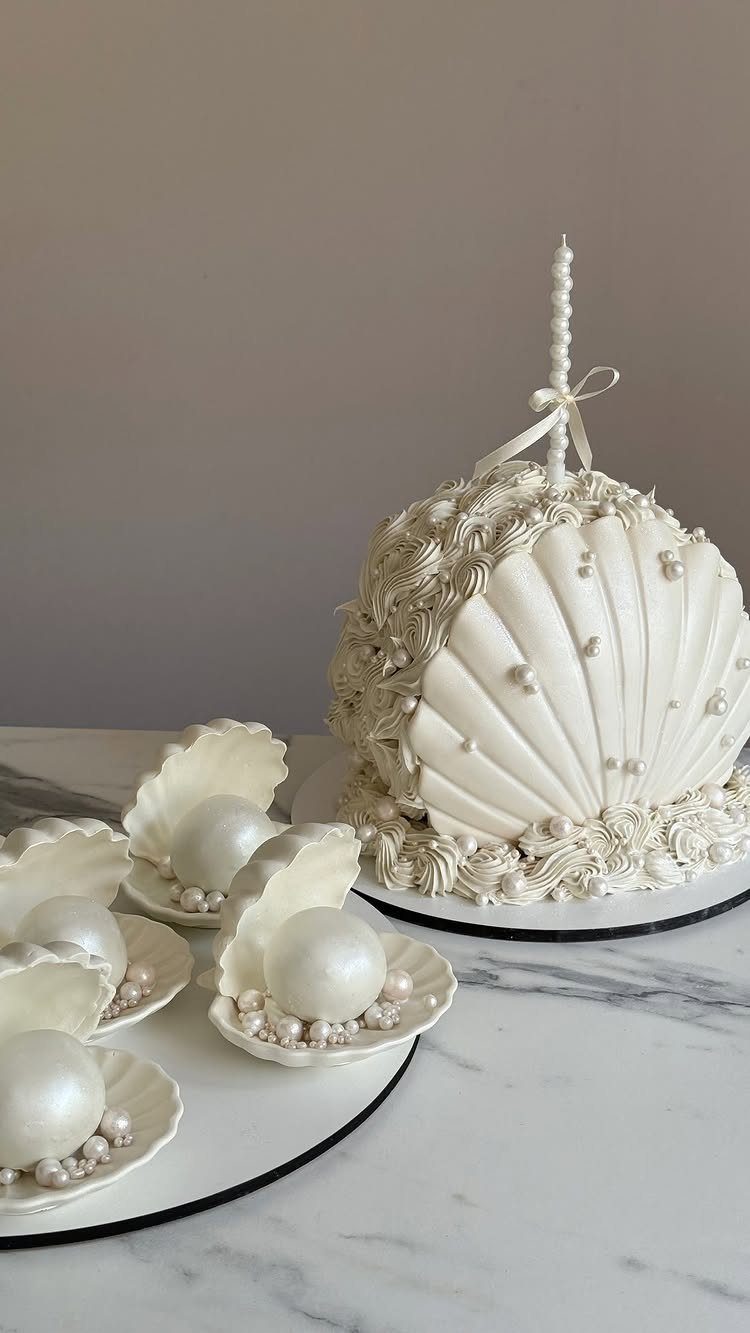 White seashell decorated cake and pearl dessert spheres on a marble tabletop.