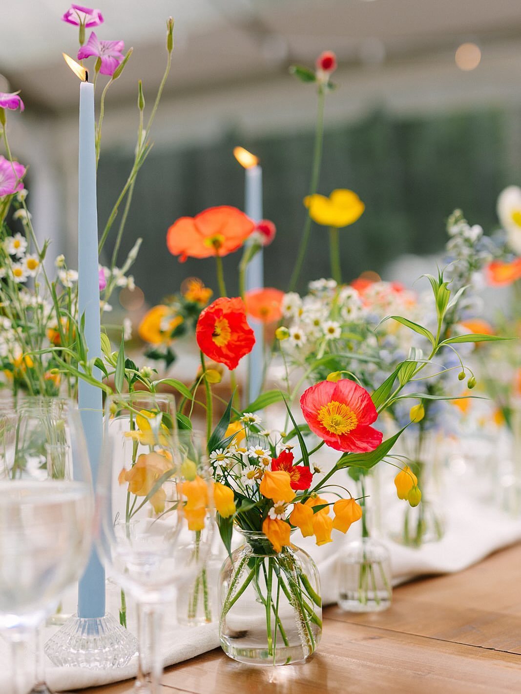 Colorful wildflowers in small glass vases arranged on a wooden table with blue taper candles.