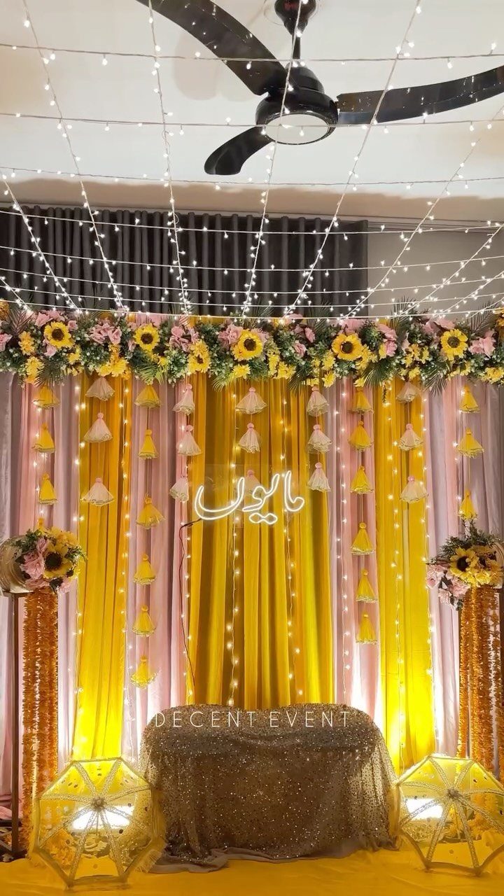 Yellow and Pink Wedding Colors: 6 Ideas for a Sunny Celebration 5 Yellow and pink draped curtains decorated with sunflowers, pink flowers, and hanging fairy lights for a wedding.