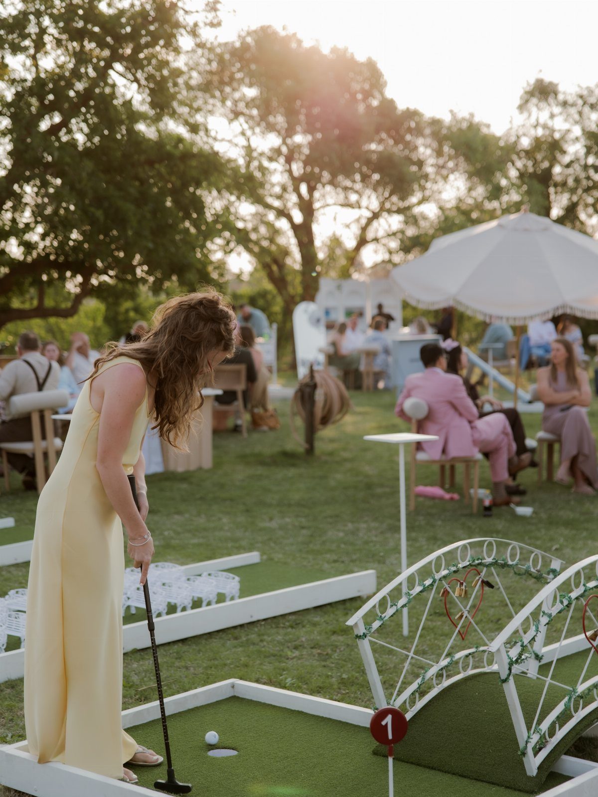 Yellow and Pink Wedding Colors: 6 Ideas for a Sunny Celebration 2 A woman in a yellow dress playing mini-golf on an outdoor course in a garden.