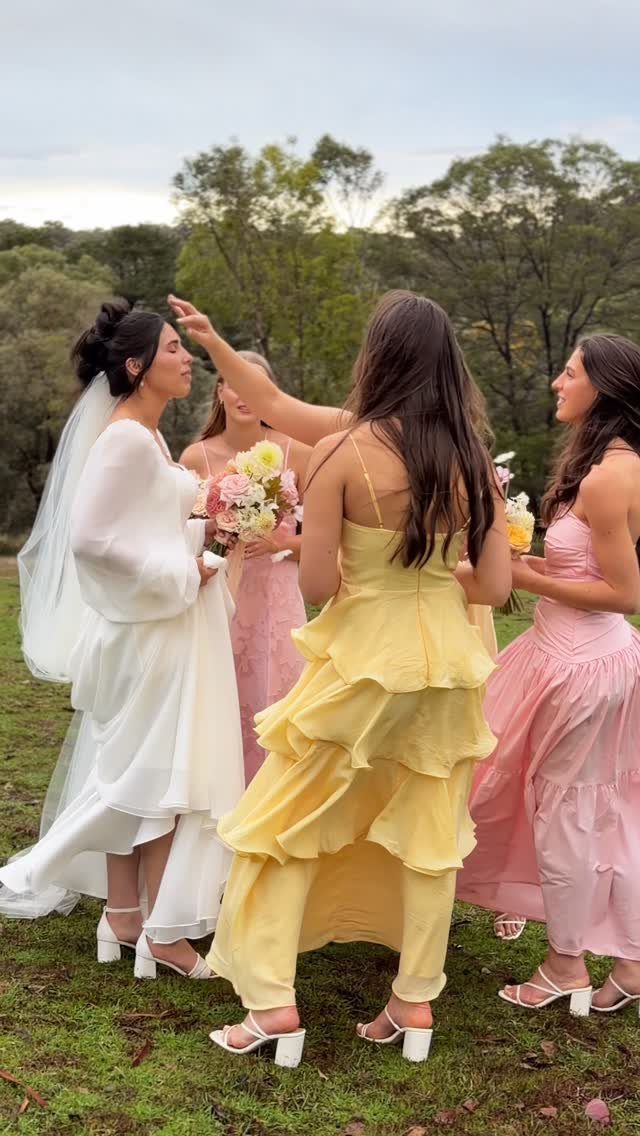 Yellow and Pink Wedding Colors: 6 Ideas for a Sunny Celebration 4 A bride in white stands with bridesmaids wearing pink and yellow dresses in a field.